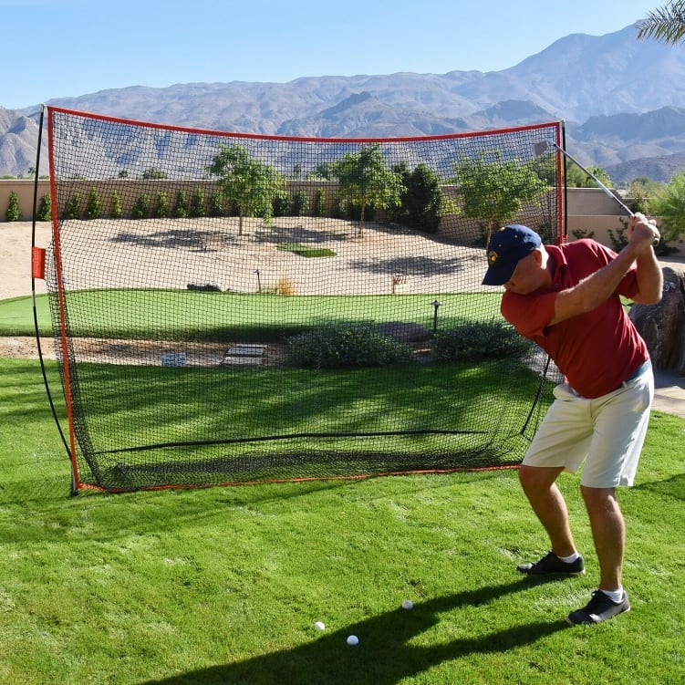 Golfer hitting a shot into a portable golf practice net in a sunny garden